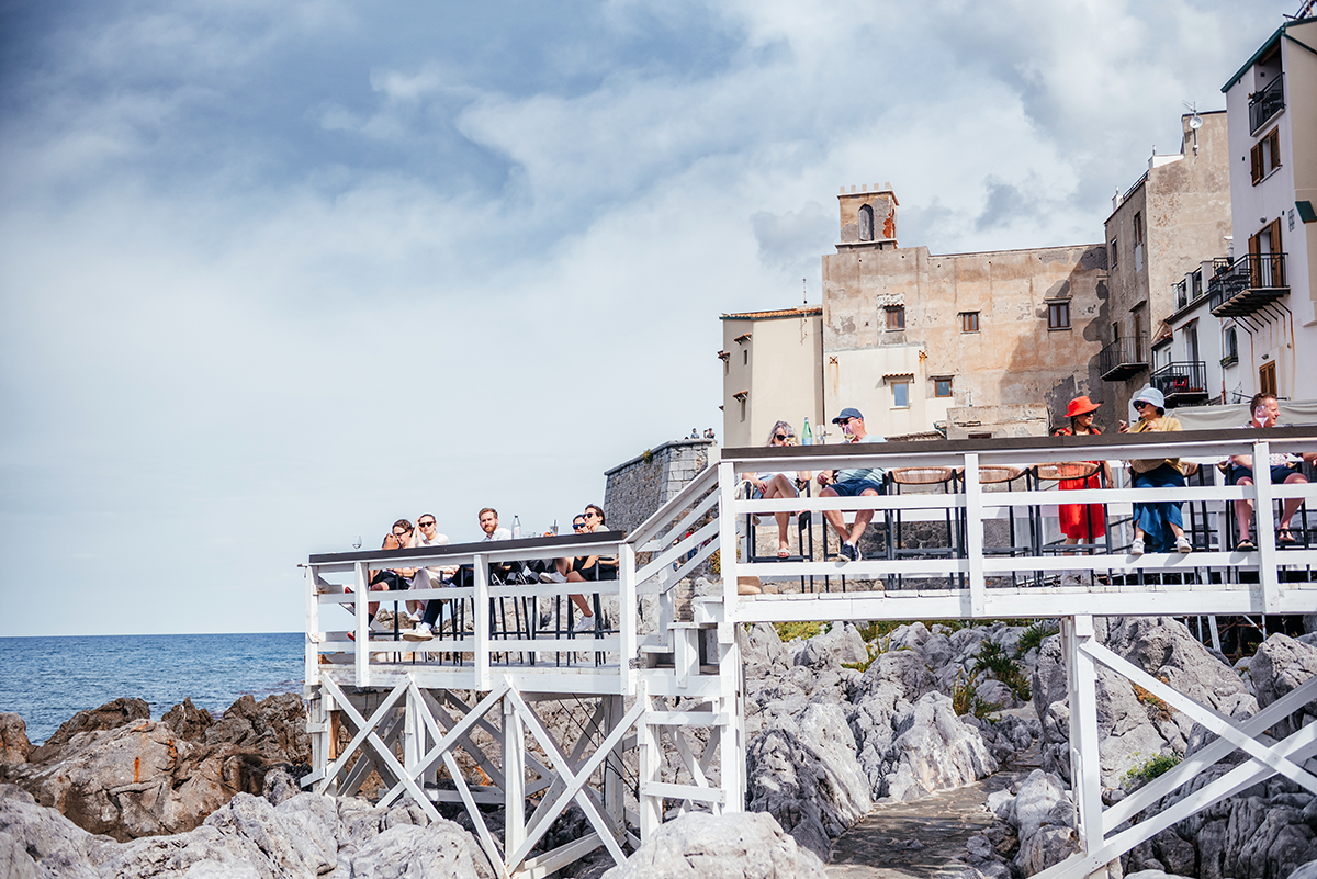 Seaside café on wooden terrace above the rocks at Al Porticciolo in Cefalù, Sicily